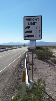 Signage on a two-lane highway depicting weight limits of large vehicles including 9 Tons, 14 Tons and 18 Tons.