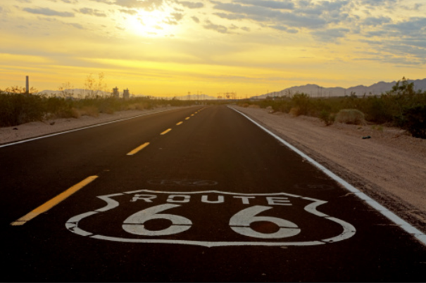 Route 66 signage painted onto road with a sunset in the background. 