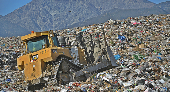 Heavy machinery climbing an incline at a waste disposal site.