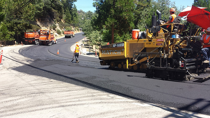 Asphalt workers smoothing out a newly laid section of road.