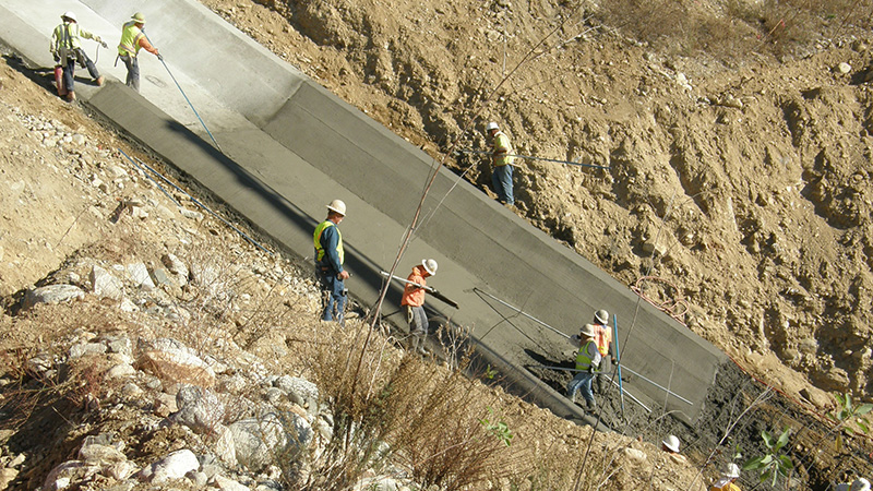 Concrete workers on an incline smoothing-out a section of wet cement.