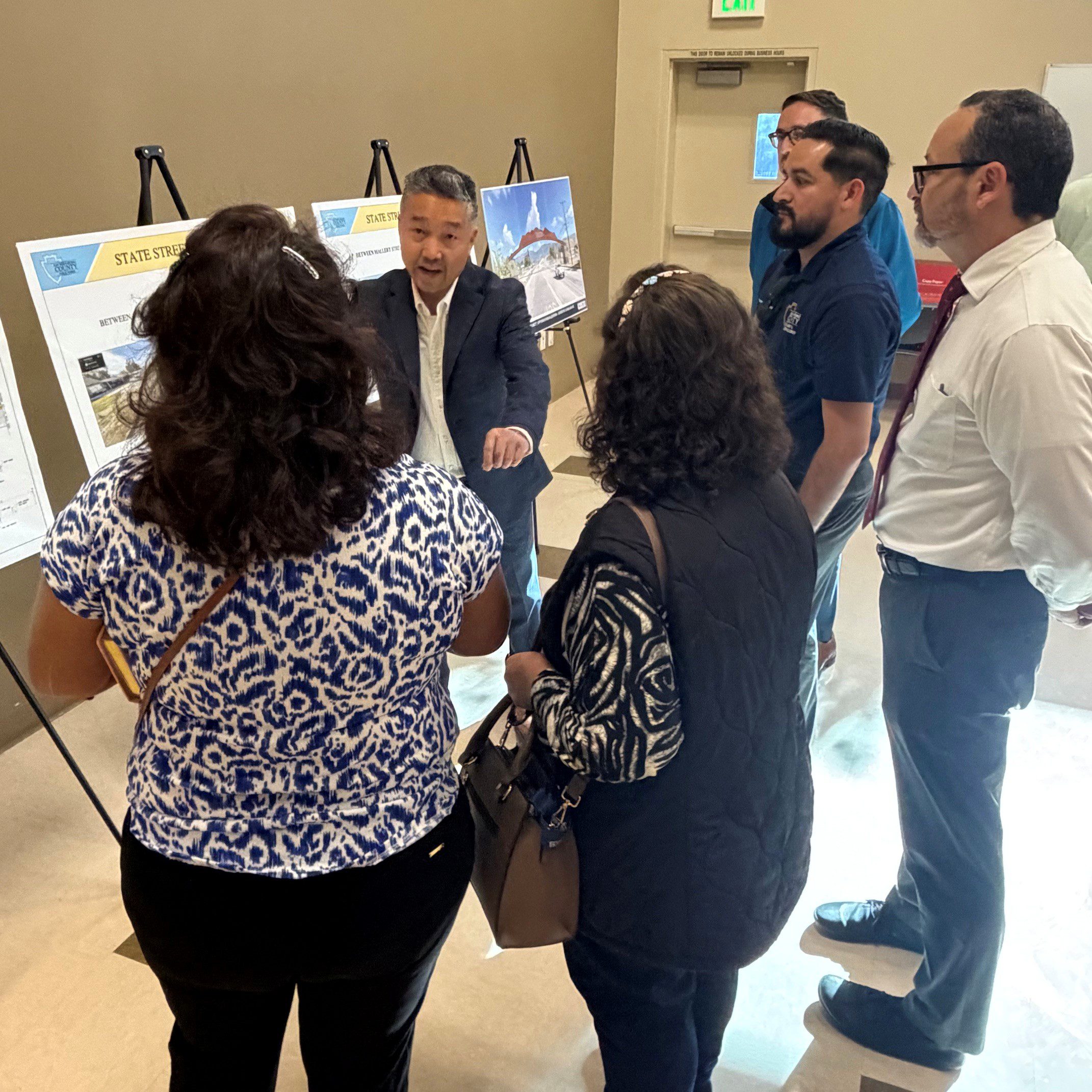 Staff and attendees gather around display boards as a speaker explains roadway improvement plans at a workshop.