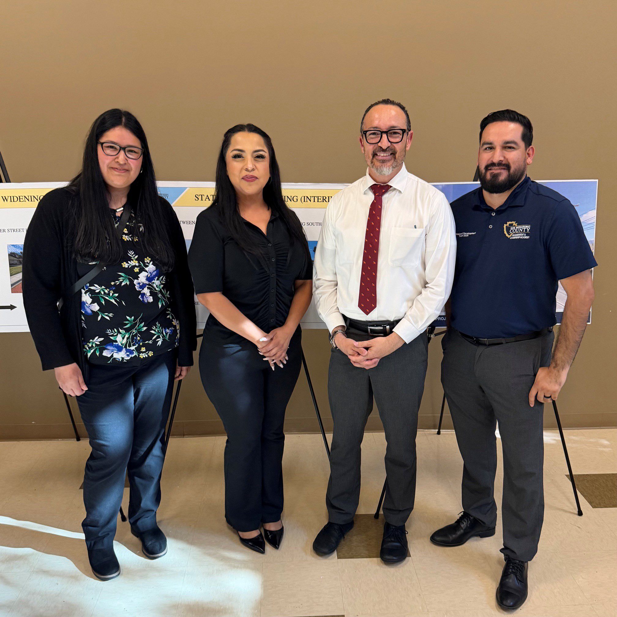 Four Public Works staff pose in front of project display boards at a San Bernardino County workshop event.