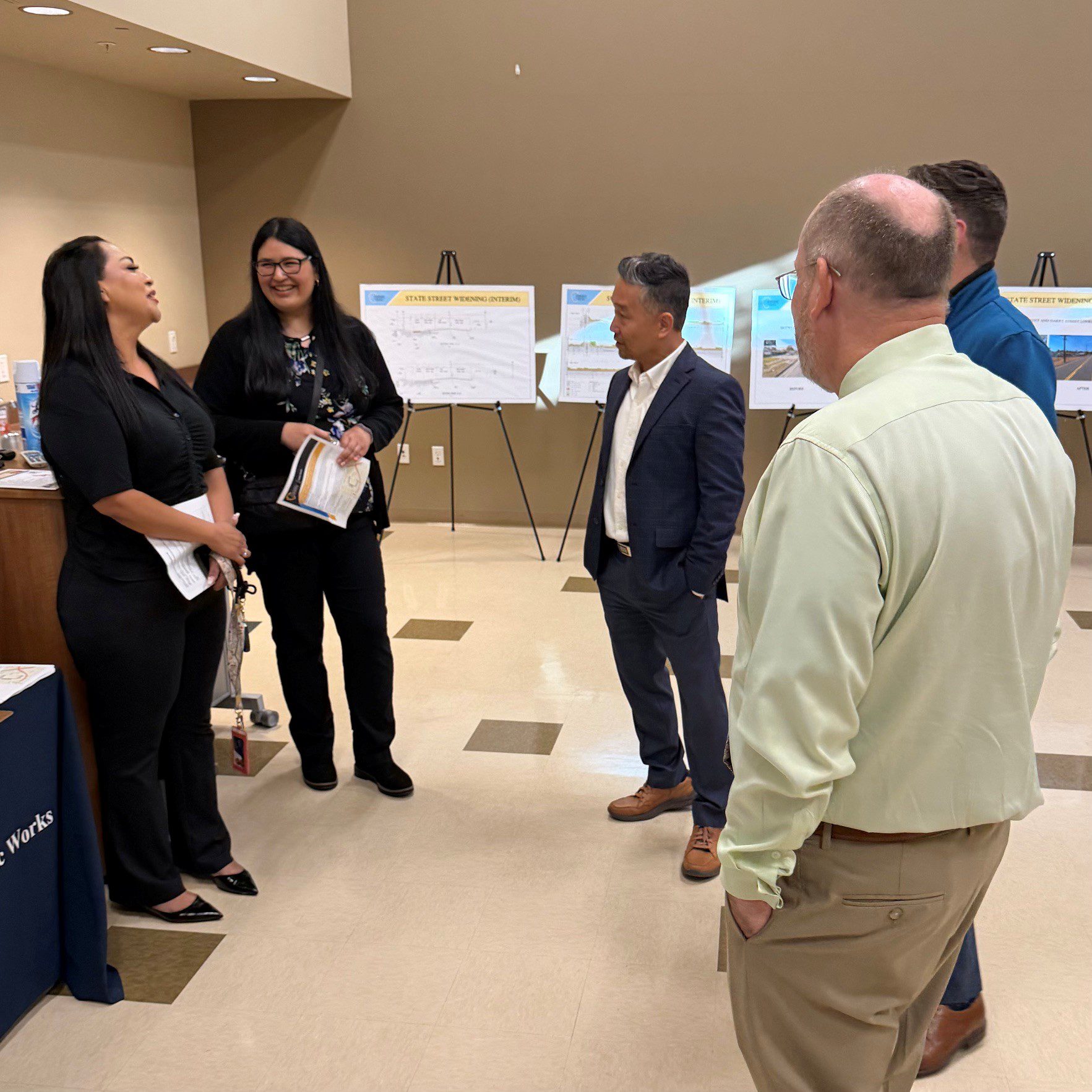 Small group conversation among staff and attendees in a room with project boards for a public works workshop.